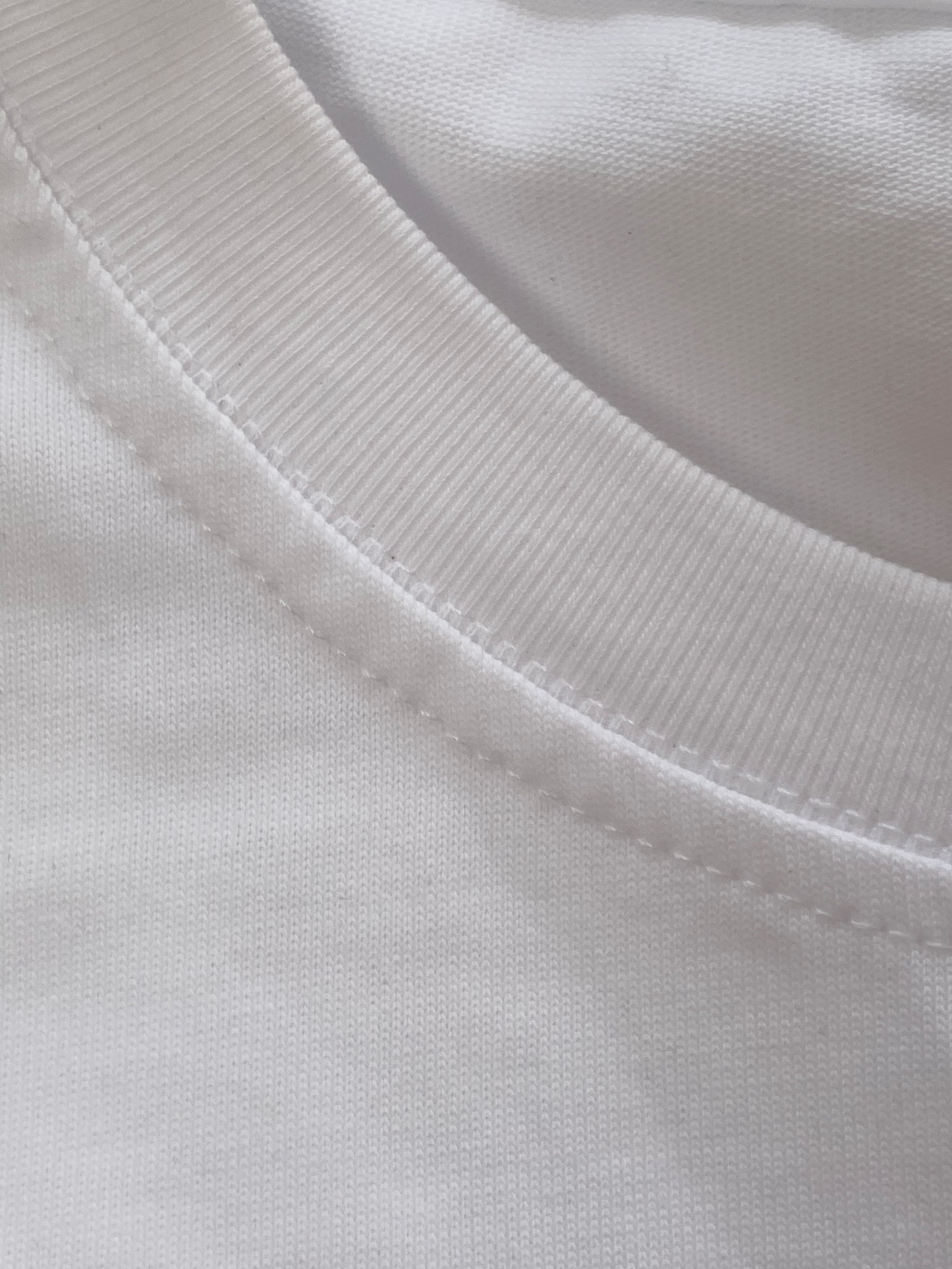 A close up photo of the texture of a white cotton t shirt around the neck line and its stitching